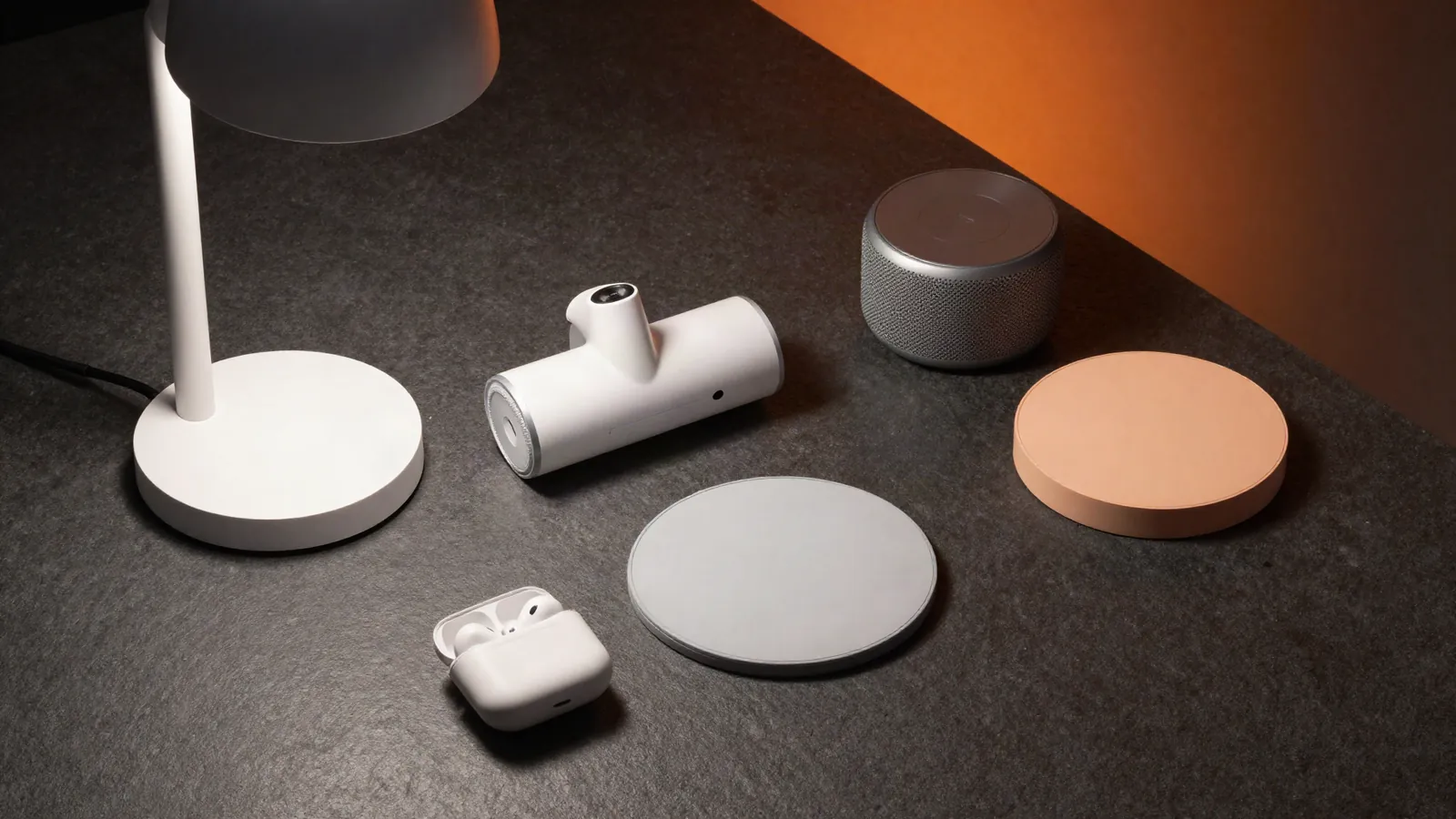 Small tech gadgets including a desk lamp, mini vacuum and wireless charger arranged on dark stone